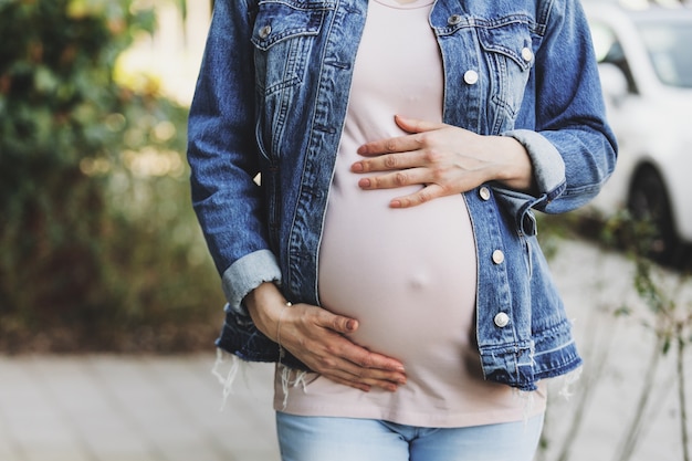 Mujer embarazada en chaqueta de jeans de pie al aire libre y tocando el vientre