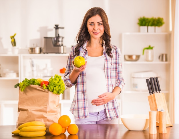 Mujer embarazada en la cocina con frutas y verduras.