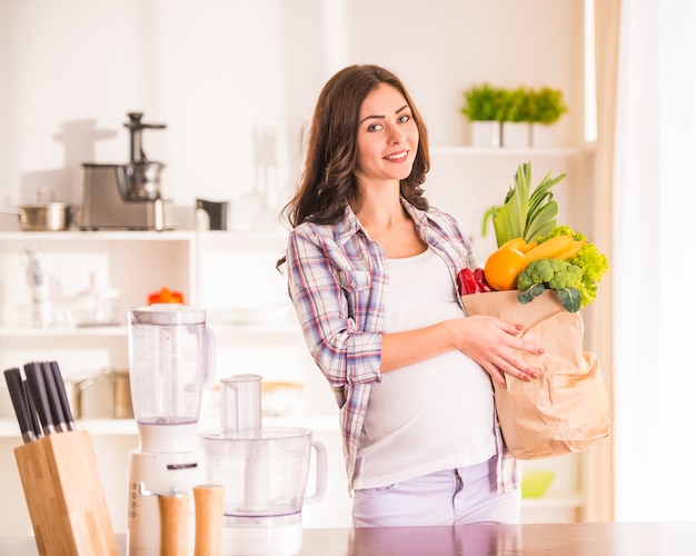 Mujer embarazada en la cocina con frutas y verduras.