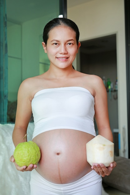 Mujer embarazada con coco y guayaba en su barriga. Concepto saludable.