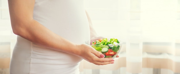 Una mujer embarazada come una ensalada con verduras.