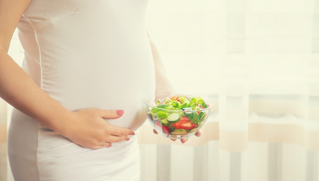 Una mujer embarazada come una ensalada con verduras.