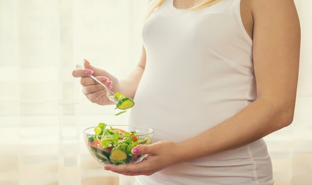 Una mujer embarazada come una ensalada con verduras.