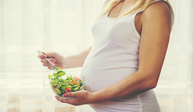 Una mujer embarazada come una ensalada con verduras.