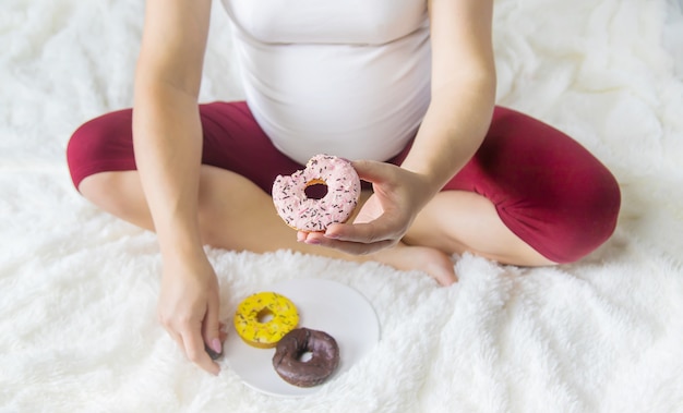 Una mujer embarazada come rosquillas dulces. Enfoque selectivo.