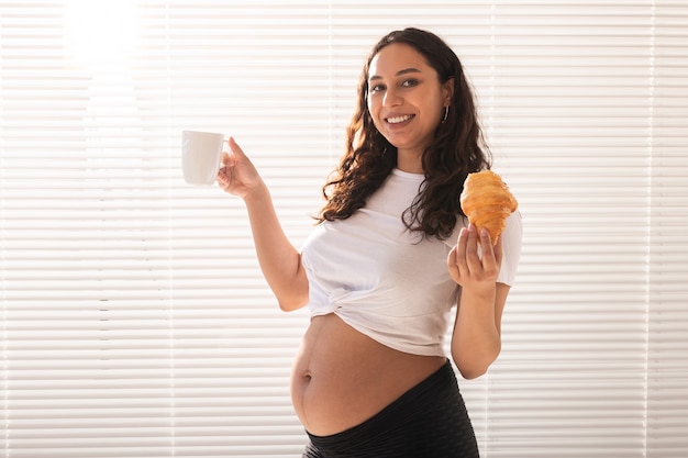 Mujer embarazada comiendo croissant y bebe café. Licencia por embarazo y maternidad