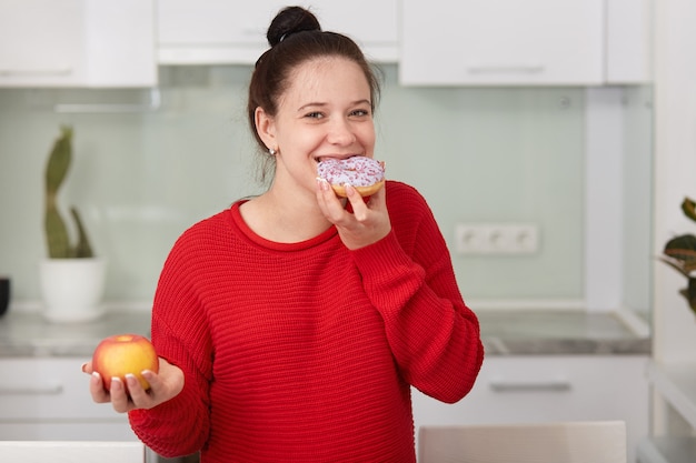 Mujer embarazada comiendo pastel dulce y sosteniendo la manzana en otra mano