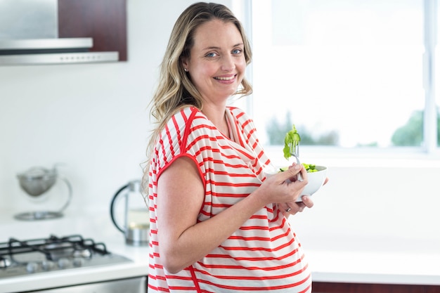 Mujer embarazada comiendo un plato de ensalada en la cocina