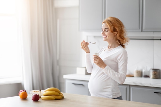Una mujer embarazada comiendo yogur en la cocina.
