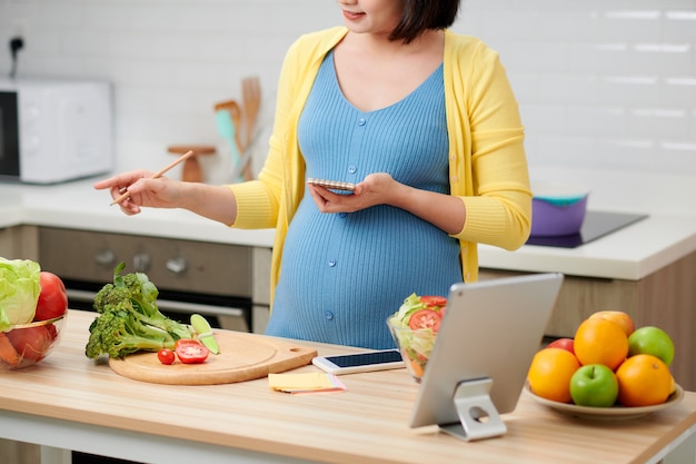 Mujer embarazada comprobando y haciendo la lista de compras antes de ir a la tienda de comestibles
