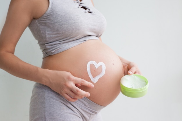 Mujer embarazada con corazón rojo y la mano sobre su vientre, símbolo de una nueva vida, concepto de esperar un bebé y extender la familia