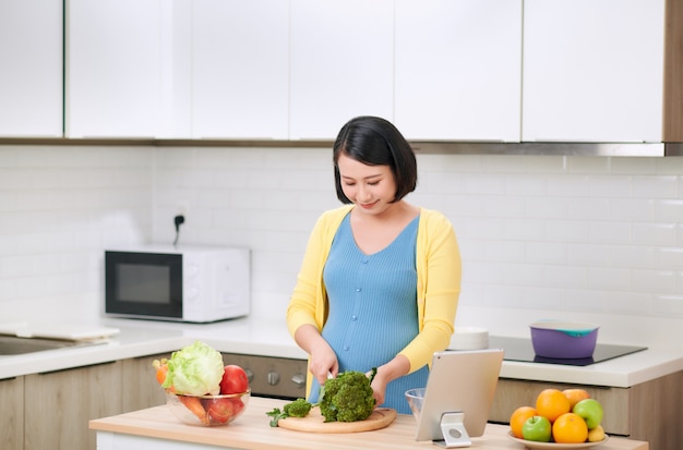 Mujer embarazada cortando brócoli para ensalada verde fresca, mujer prepara sabrosa cena orgánica en casa