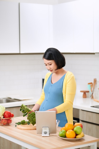 Mujer embarazada cortando brócoli para ensalada verde fresca, nutrición saludable para la futura madre