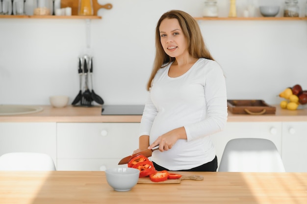 Mujer embarazada cortando verduras en casa en la cocina