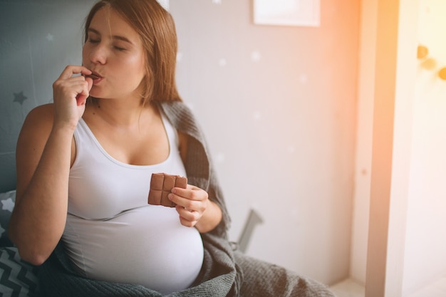 Mujer embarazada disfrutando de comer chocolate en casa