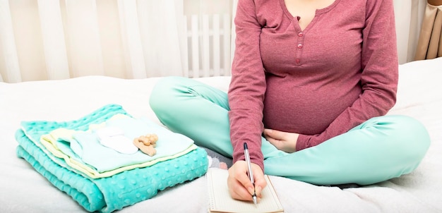 Mujer embarazada empacando ropa de bebé para la atención del hospital de maternidad Mujer tomando notas