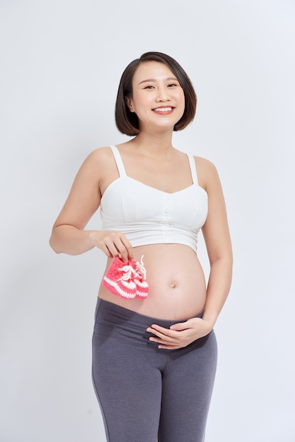 Mujer embarazada de ensueño con patucos de bebé cerca de la barriga en blanco