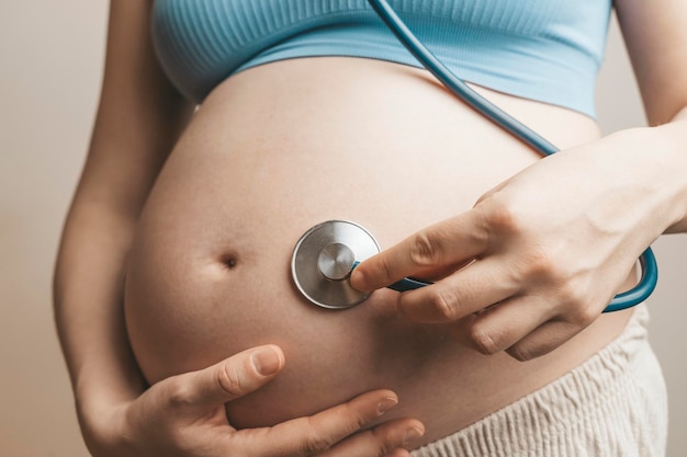 La mujer embarazada escucha los latidos del corazón y los movimientos del bebé con un estetoscopio o fetoscopio o Cuerno de Pinard. Salud fetal prenatal, ansiedad, concepto de miedo. foto de alta calidad