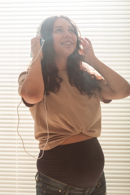 Mujer embarazada escucha música en auriculares en casa y bailes