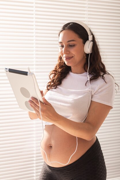 Mujer embarazada escuchando música en auriculares con tableta digital