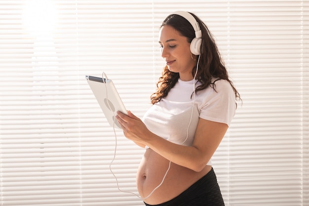 Mujer embarazada escuchando música en auriculares con tableta