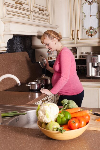 La mujer embarazada está cocinando platos en la cocina