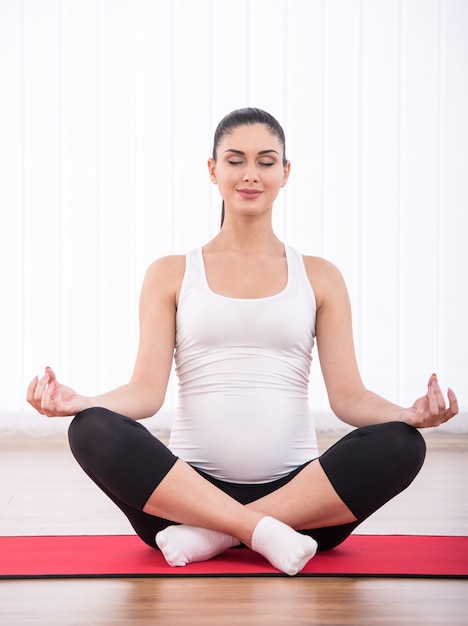 La mujer embarazada está haciendo ejercicio de yoga en colchonetas de yoga.