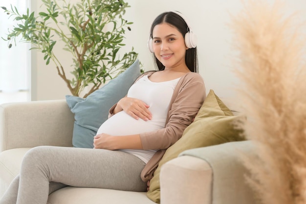 Mujer embarazada feliz con auriculares escuchando música de Mozart y acostada en el sofá concepto de embarazo