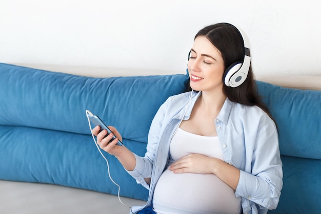 mujer embarazada feliz escuchando música en auriculares y tocando su vientre conceptos de tecnología de personas embarazadas