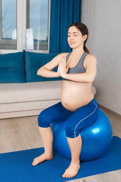 mujer embarazada feliz haciendo ejercicio en casa madre embarazada medita en la pelota de ajuste embarazo yoga concepto de estilo de vida saludable