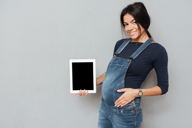 Mujer embarazada feliz que muestra la pantalla de la tableta