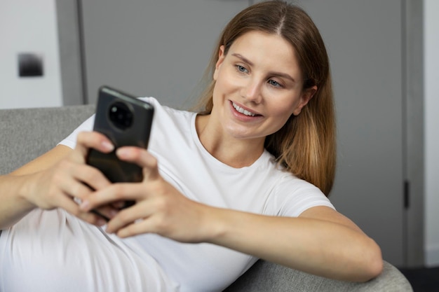 Mujer embarazada feliz que usa un teléfono inteligente para comprar en línea en casa