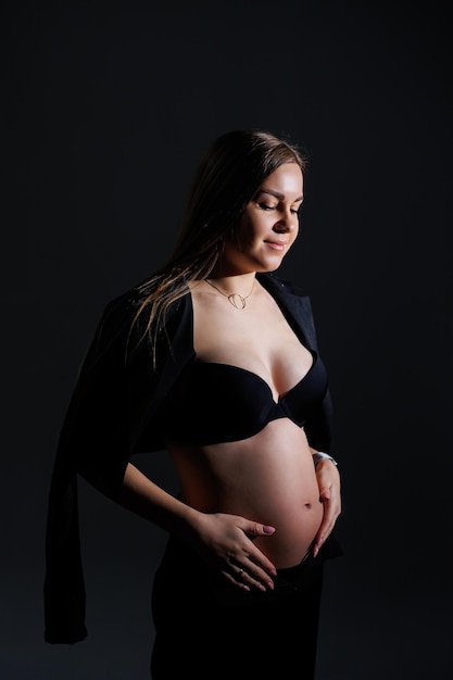 Mujer embarazada feliz en un traje negro sobre un fondo gris Hermosa mujer embarazada elegante Fotos de estudio suave de una mujer embarazada