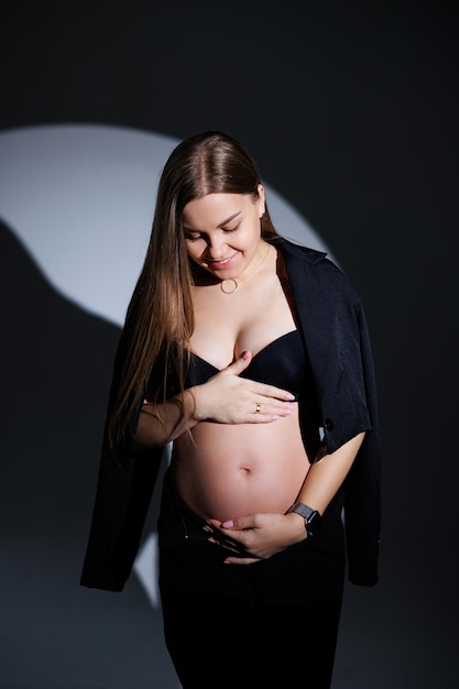 Mujer embarazada feliz en un traje negro sobre un fondo gris Hermosa mujer embarazada elegante Fotos de estudio suave de una mujer embarazada