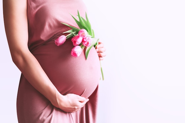 Mujer embarazada con flores tiene las manos sobre el vientre en el concepto de vacaciones del día de la madre de fondo blanco