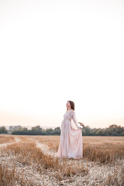 Una mujer embarazada en el fondo de un campo al atardecer una mujer con el pelo largo y el vientre extendió los brazos a los lados y disfruta de la libertad del viento