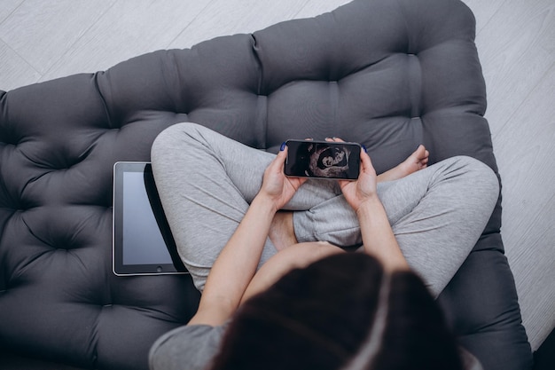 Mujer embarazada con foto de ultrasonido sentada en la cama