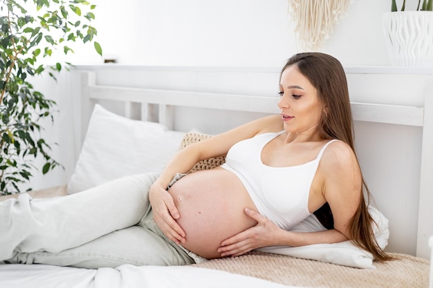 Una mujer embarazada con una gran barriga abierta en una cama en casa sueña con tener un bebé La futura madre está esperando y preparándose para el nacimiento de un niño en un dormitorio luminoso