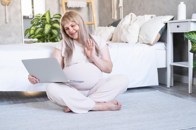 mujer embarazada con gran barriga embarazo avanzado usando una computadora portátil sentada en el piso
