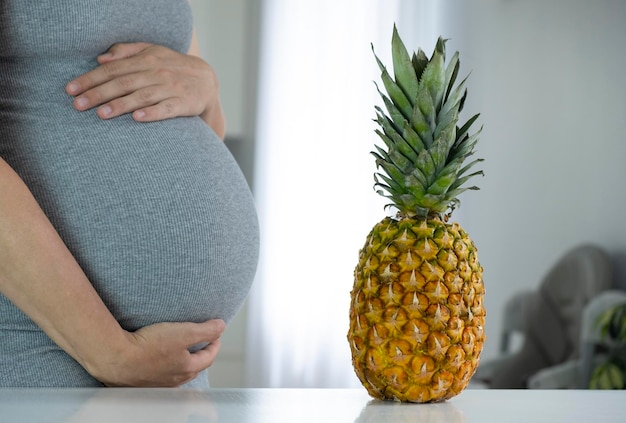 Mujer embarazada con gran barriga y gran piña fresca en el interior de la casa