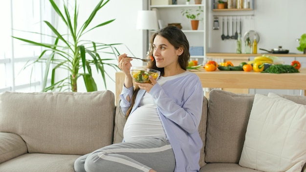 Foto mujer embarazada con gran placer comiendo ensalada de verduras en el sofá