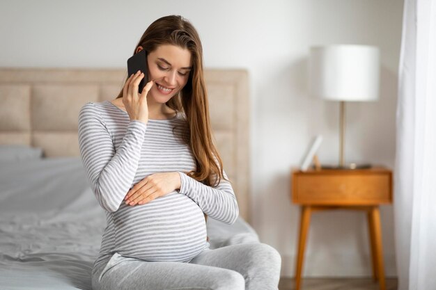 Foto mujer embarazada hablando por teléfono en el dormitorio.