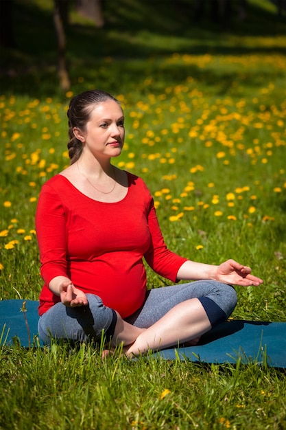 Mujer embarazada haciendo asana sukhasana al aire libre