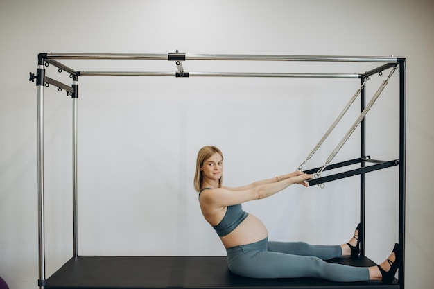 Mujer embarazada haciendo ejercicio con la ayuda del reformador en clase de pilates