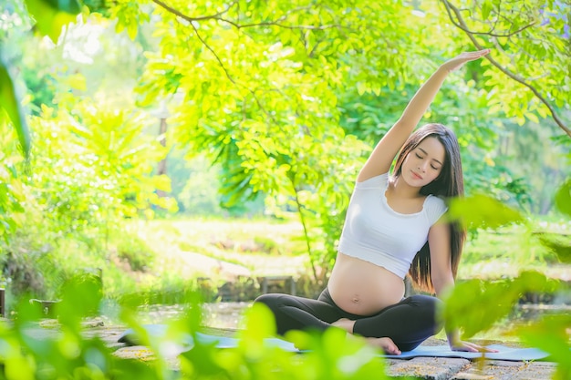 Mujer embarazada haciendo ejercicio de yoga en la naturaleza en verano