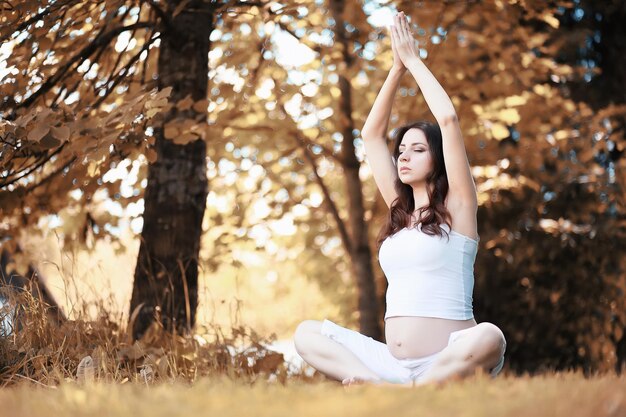 Mujer embarazada haciendo ejercicio de yoga en otoño