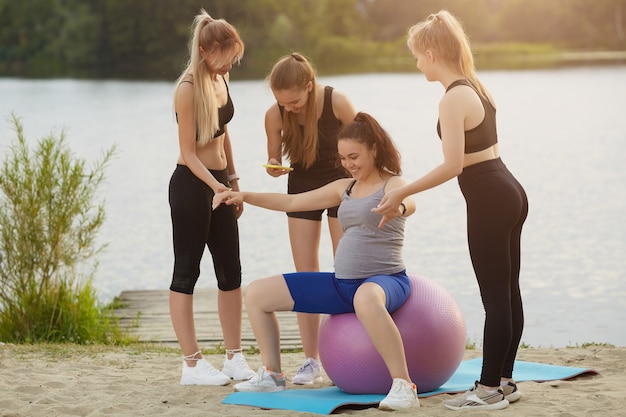 Mujer embarazada haciendo ejercicios de fitness con una pelota con un entrenador y amigos