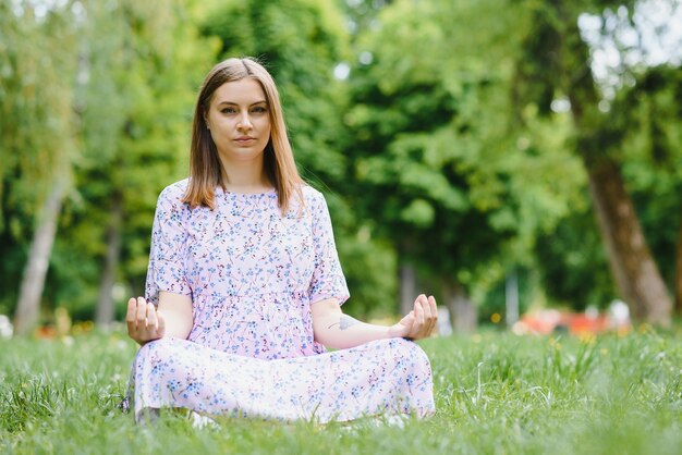 Mujer embarazada haciendo yoga en el parque. sentado en la hierba.