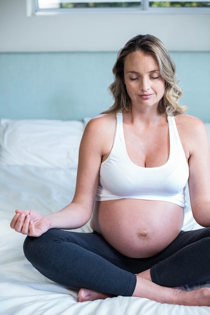 Mujer embarazada haciendo yoga en su cama