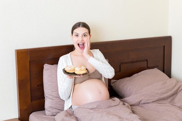 Mujer embarazada hambrienta está comiendo deliciosos postres quedándose en la cama en casa Disfrutando de comida dulce durante el concepto de embarazo